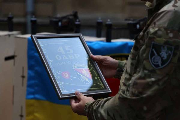 Руки військовослужбовця в камуфляжі тримають рамку із пам'ятною символікою 45 ОАБр